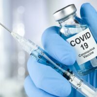 Healthcare cure concept with a hand in blue medical gloves holding Coronavirus, Covid 19 virus, vaccine vial
